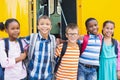 Smiling kids standing arm around in front of school bus Royalty Free Stock Photo