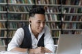 Smiling Korean guy sit in library studying online using laptop Royalty Free Stock Photo