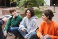 Smiling lady with dark curly hair sitting with her friends in courtyard of university. Group of cool students spending