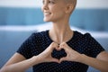 Smiling lady diagnosed with cancer holding fingers joined in heart