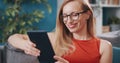 Smiling lady sitting on couch and looking at tablet screen