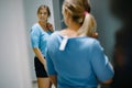 Smiling lady standing in front of mirror, admiring reflection while trying on new blue t-shirt in dressing room.