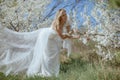 Smiling Lady in wedding gown stand near cherry blossom, lean over branch, going to take shoes on ramification of tree.