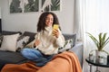 Smiling latin girl sitting on couch using cell phone in living room at home. Royalty Free Stock Photo