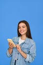 Happy Latin teen girl wearing denim using phone on blue background. Vertical. Royalty Free Stock Photo