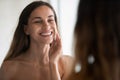 Smiling Latin woman look in bath mirror clean face
