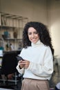 Smiling latin young business woman using mobile phone standing in office. Royalty Free Stock Photo