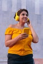 Smiling Latina mature woman using cell phone while listening to music with headphones in the street Mature Latina woman using cell Royalty Free Stock Photo