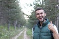 A smiling and laughing brunette holding a thumbs up in approval while standing in the middle of a forest hike. The great outdoors