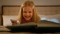 Smiling laughing cute little Caucasian girl preschooler child kid daughter reading book using flashlight in evening Royalty Free Stock Photo