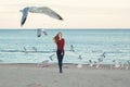 Smiling laughing excited Caucasian young woman in jeans running jumping among seagulls birds