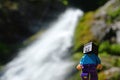 Smiling LEGO Minecraft figure of Steve in front of tall narrow mountain waterfall defocused in background.