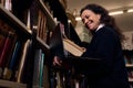 Smiling librarian holding a book inside a library surrounded by shelves of books Royalty Free Stock Photo