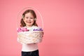 Smiling litle girl holding a wicker basket of tender white, pink and purple flowers isolated over pink background Royalty Free Stock Photo