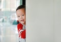 Smiling little Asian baby boy hide behind a corner room. Small children playing peekaboo game indoor. What a surprise