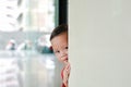 Smiling little Asian baby boy hide behind a corner room. Small children playing peekaboo game indoor. What a surprise