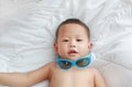 Smiling little Asian baby boy try wearing sunglasses lying on white blanket on bed. Above view Royalty Free Stock Photo
