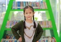 Smiling little Asian child girl against bookshelf at library. Children creativity and imagination concept