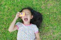 Smiling little Asian child girl with digital camera lying on green lawn background