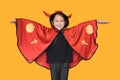 Smiling little Asian child girl dressed Halloween costume. Kid in red Dracula robe isolated on yellow background