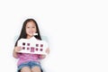 Smiling little Asian child girl holding mock-up paper school sitting on kid chair isolated over white background. Education and Royalty Free Stock Photo