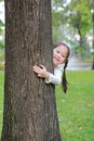 Smiling little Asian child girl hugging a big tree in the garden with hide her body behind trunk Royalty Free Stock Photo