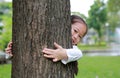 Smiling little Asian child girl hugging a big tree in the garden with hide her body behind trunk Royalty Free Stock Photo