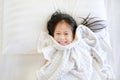 Smiling little Asian child girl lying on bed with blanket and looking at camera. Above view Royalty Free Stock Photo