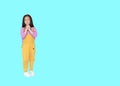 Smiling little Asian child girl in pink-yellow dungarees expression hands implore isolated over cyan background with copy space