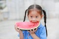 Smiling little Asian child girl in school uniform enjoy eating watermelon outdoors Royalty Free Stock Photo