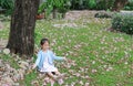 Smiling little Asian child girl sitting on green grass under tree trunk with falling pink flower in the park garden Royalty Free Stock Photo
