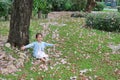 Smiling little Asian child girl sitting on green grass under tree trunk with falling pink flower in the park garden Royalty Free Stock Photo