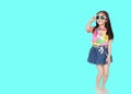 Smiling little Asian child girl wearing a floral pattern summer dress and sunglasses isolated on cyan background with copy space. Royalty Free Stock Photo