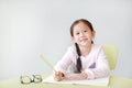 Smiling little Asian child girl write in a book or notebook with pencil sitting on kid chair and table against white background Royalty Free Stock Photo