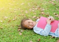 Smiling little Asian girl with book lying on green grass with dried leaves in the summer garden Royalty Free Stock Photo