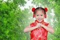 Smiling little asian girl in cheongsam respecting on traditional chinese new year festival against bamboo background