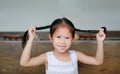 Smiling little Asian girl holding her pigtails hair lying on the wood table with looking at camera Royalty Free Stock Photo