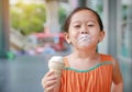 Smiling little Asian kid girl enjoy eating ice cream cone with stains around her mouth Royalty Free Stock Photo