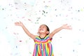 Smiling little Asian kid girl with many falling colorful tiny confetti pieces on white background. Happy New Year or