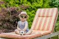 Smiling little baby boy is sitting on the deck chair holding little soccer balloon Royalty Free Stock Photo