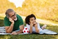 Smiling little black boy, old caucasian man lie on plaid with soccer ball, dream, look at empty place Royalty Free Stock Photo