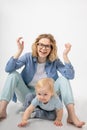 Smiling little blond blue-eyed girl daughter leaning on hands near young funny beautiful woman mother raising hands. Royalty Free Stock Photo