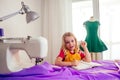 Smiling little blonde girl at the table with sewing machine with manikin Royalty Free Stock Photo