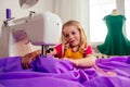 Smiling little blonde girl at the table with sewing machine with manikin Royalty Free Stock Photo