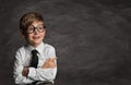 Smiling Little Boy in Glasses over School Black Board. Funny Happy Child with crossed Arms pointing Finger to Copy Space