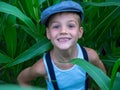 Smiling little boy with a hat and suspenders in a garden surrounded by leaves under sunlight Royalty Free Stock Photo