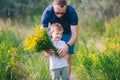 Smiling little boy and his father enjoying outdoors in field of wildflowers