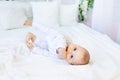 A smiling little boy lying on a white bed, hands in his mouth. space for text. Teething Royalty Free Stock Photo