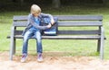 Smiling little boy opening his backpack. Child sitting on a wooden bench. Outdoor. Education, school concept Royalty Free Stock Photo
