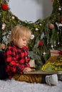 Smiling little boy reading a book near the Christmas tree. Child sitting near Xmas tree at home. Gentleman. Family Royalty Free Stock Photo